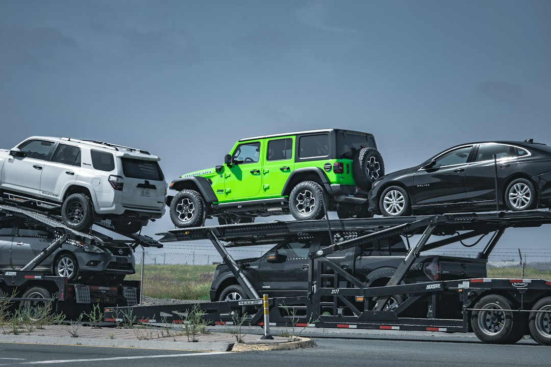 Plusieurs véhicules sur un camion porte-voitures, dont un véhicule vert au centre